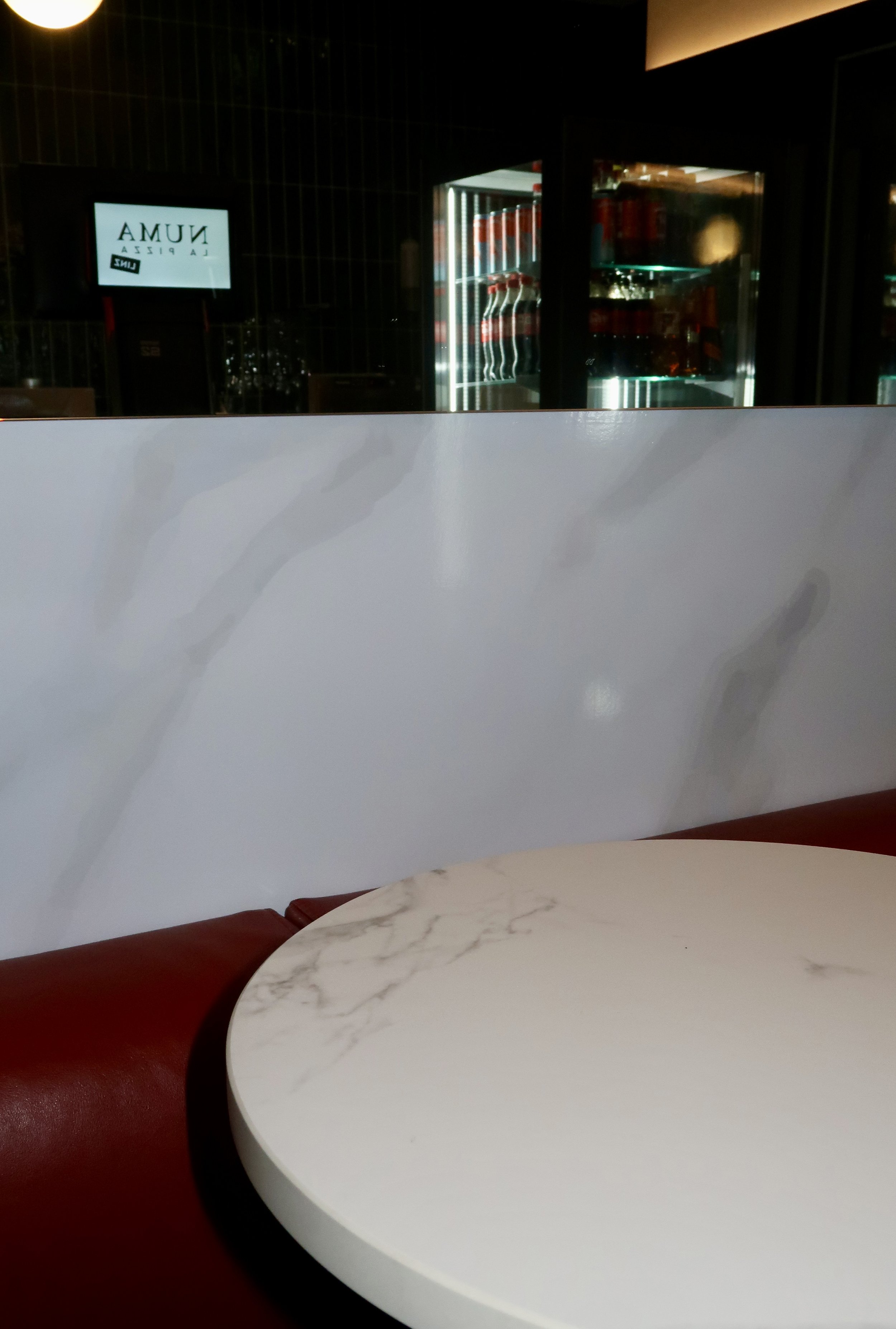 Ein Restaurant mit weißen Tischen, roten Sitzbänken und aussenansicht bei Nacht.