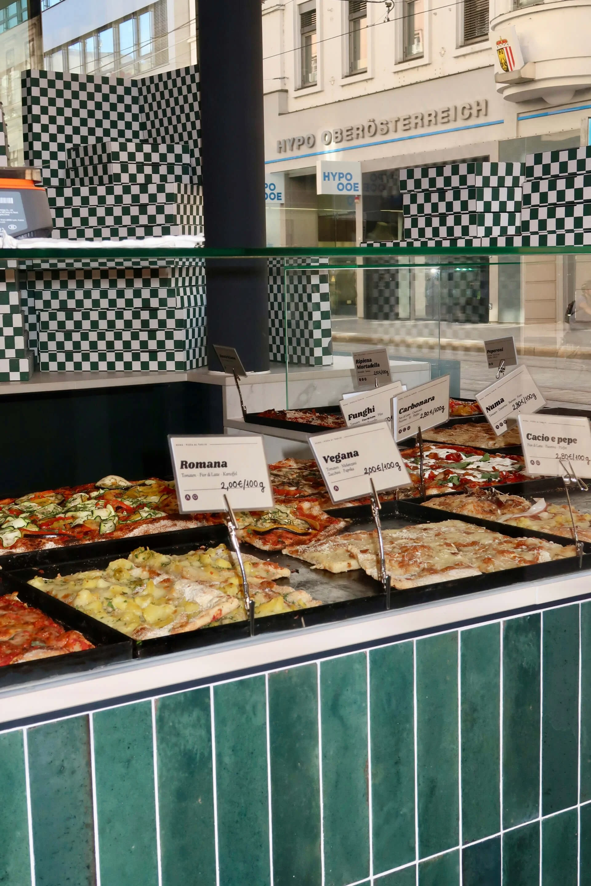 Theke mit frischen Pizza-al-Taglio-Blechen und Preisschildern bei NUMA la Pizza in Linz