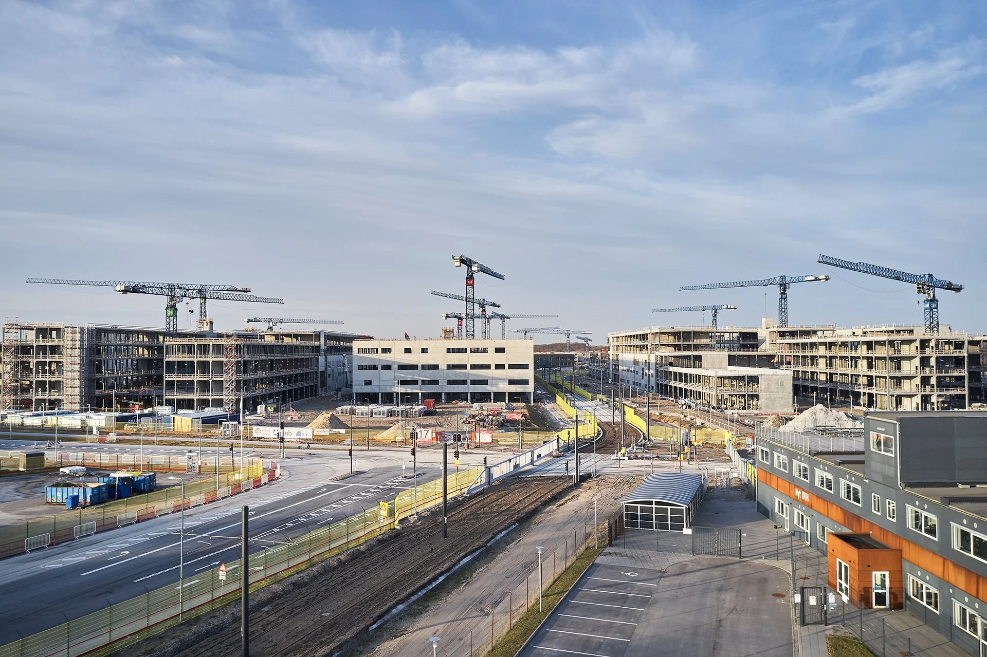 Wide view of a large construction site with multi-story buildings, several tower cranes, and surrounding roads.