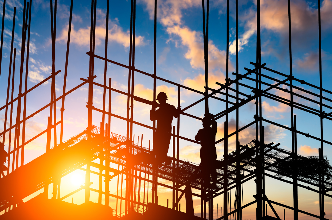 Silhouettes of two construction workers standing on scaffolding during sunset at a construction site.
