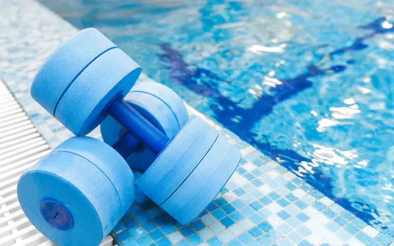 Two light blue dumbbells placed on the edge of a swimming pool with blue tile flooring.