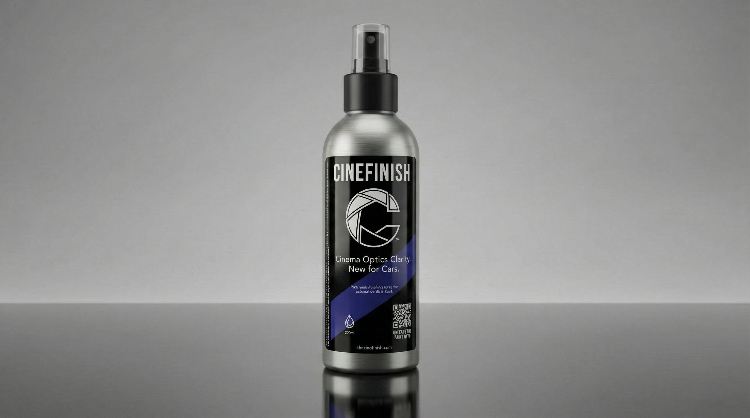 A spray bottle labeled 'CINEFINISH' with a black, white, and blue design, placed on a reflective surface against a gray background.