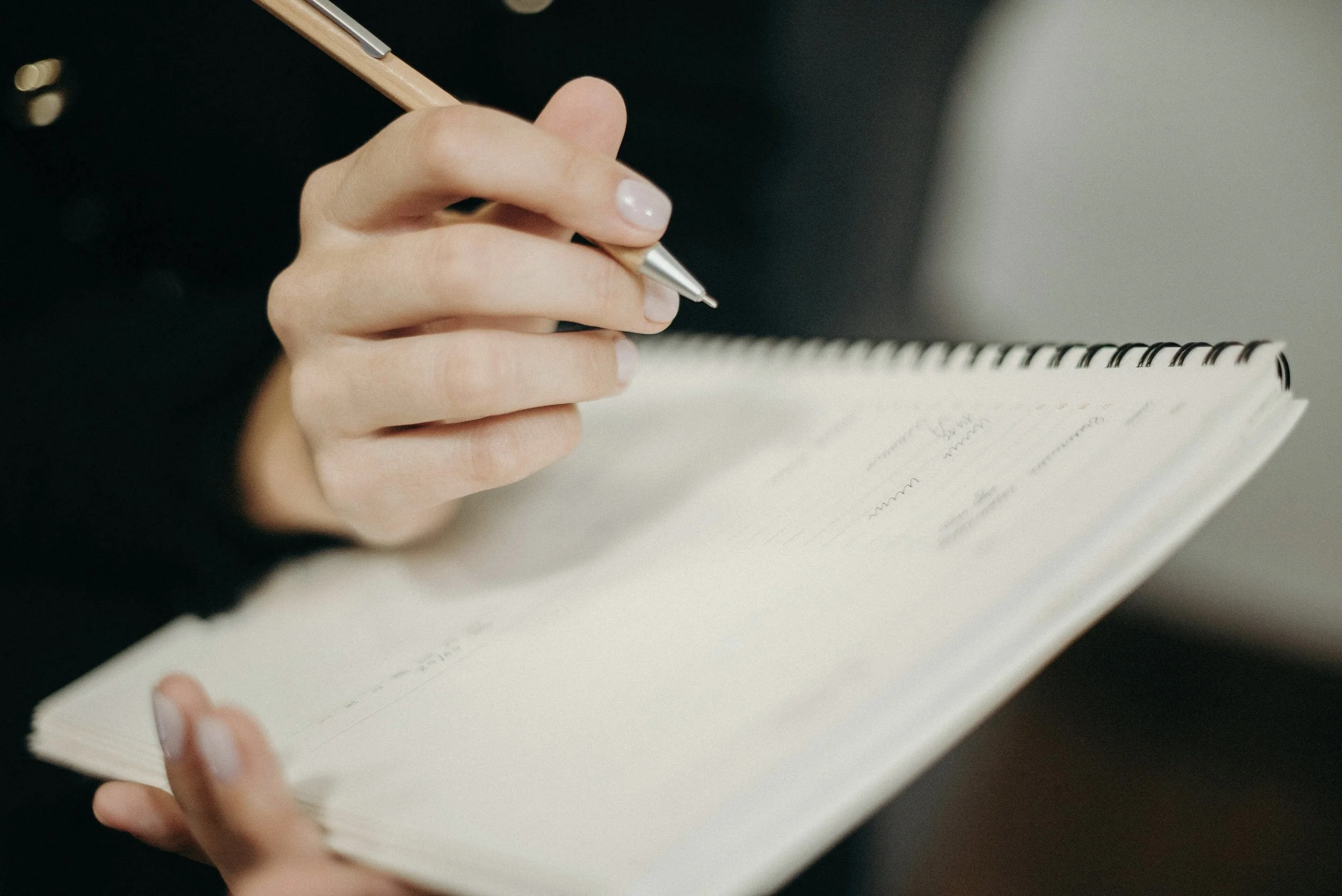 Hand mit Stift schreibt in ein Notizbuch – Sinnbild für Reflexion und Selbstfürsorge im Alltag.