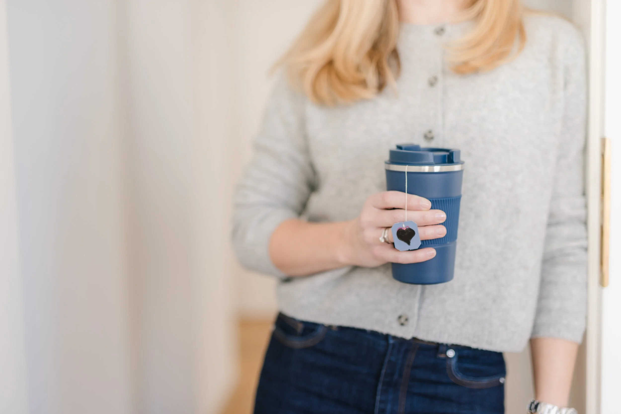 Frau hält einen blauen Becher mit Teebeutel drinnen.