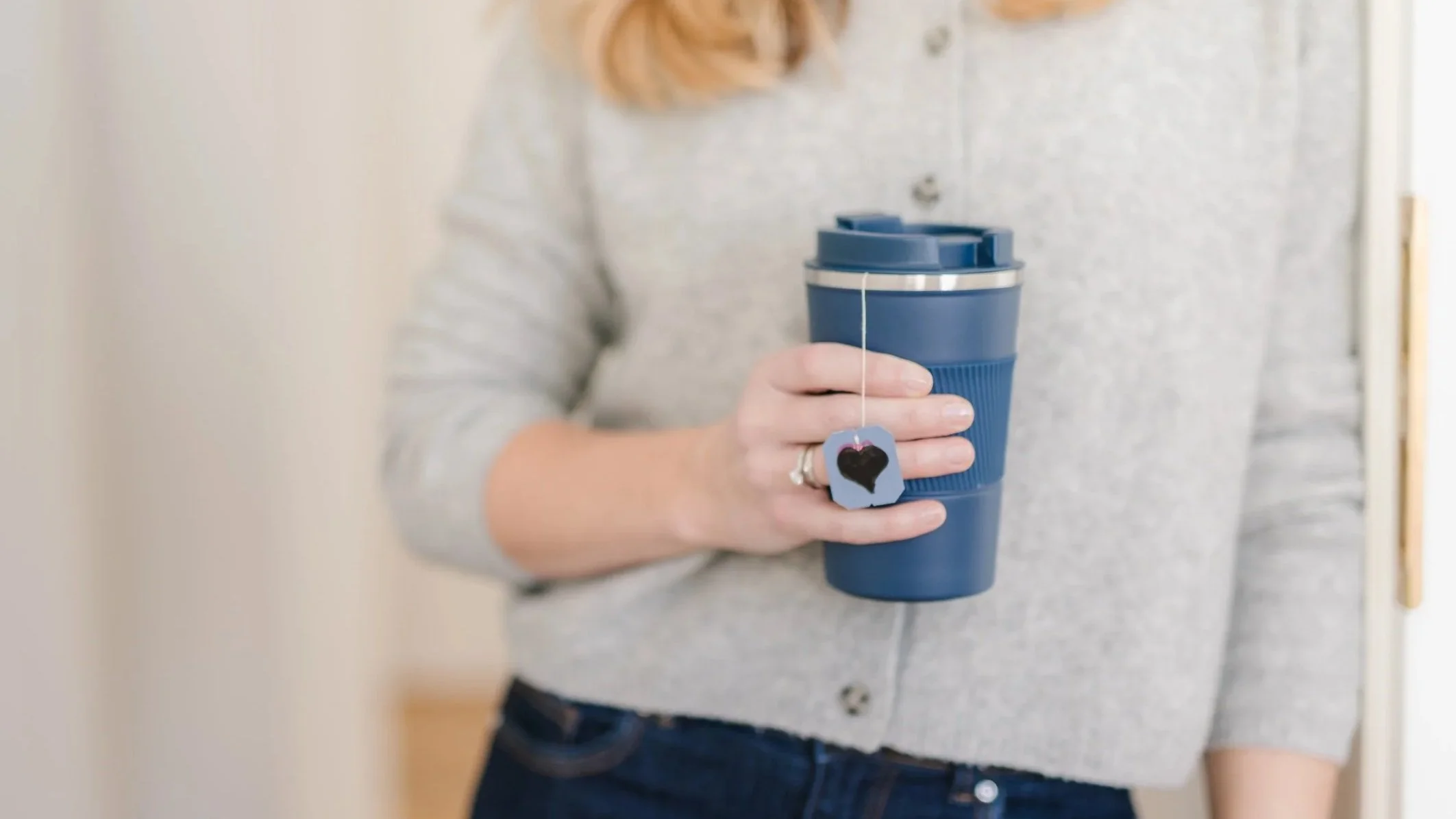 Eine Person hält einen blauen Reisebecher mit einem Teebeutel daran.