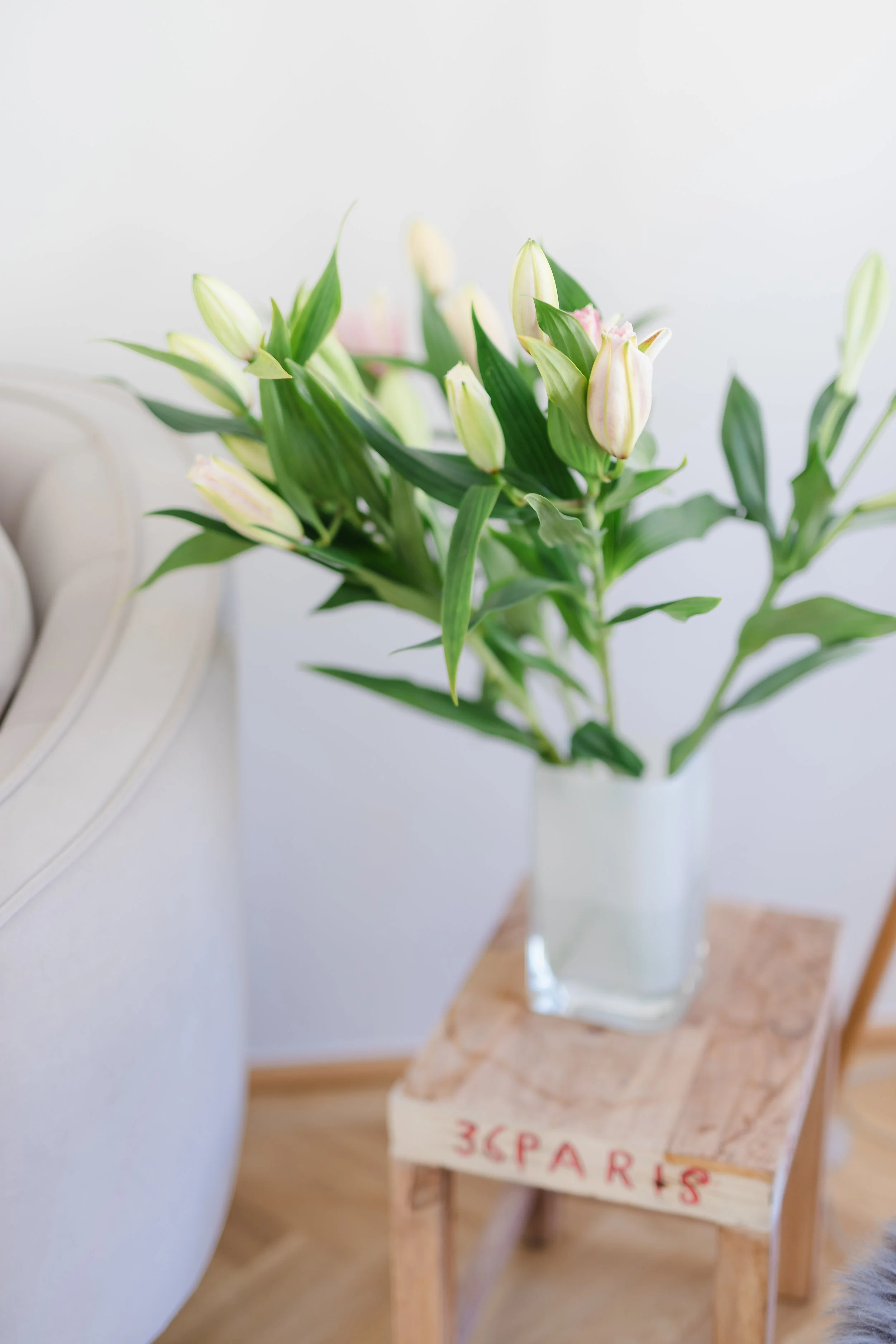 Blumenvase mit weißen und pinken Tulpen auf einem kleinen Holztisch in einem Raum.