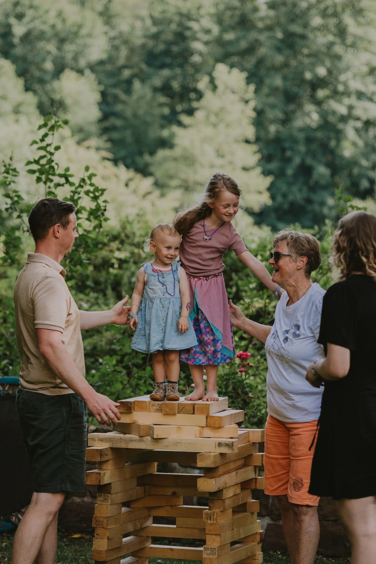 Familie auf einem von Kindern gebauten Holz-Bauwerk im Garten, Kinder auf dem Holz werden von Vater und Oma gestützt zur Einschulung feiern in der Pfalz.