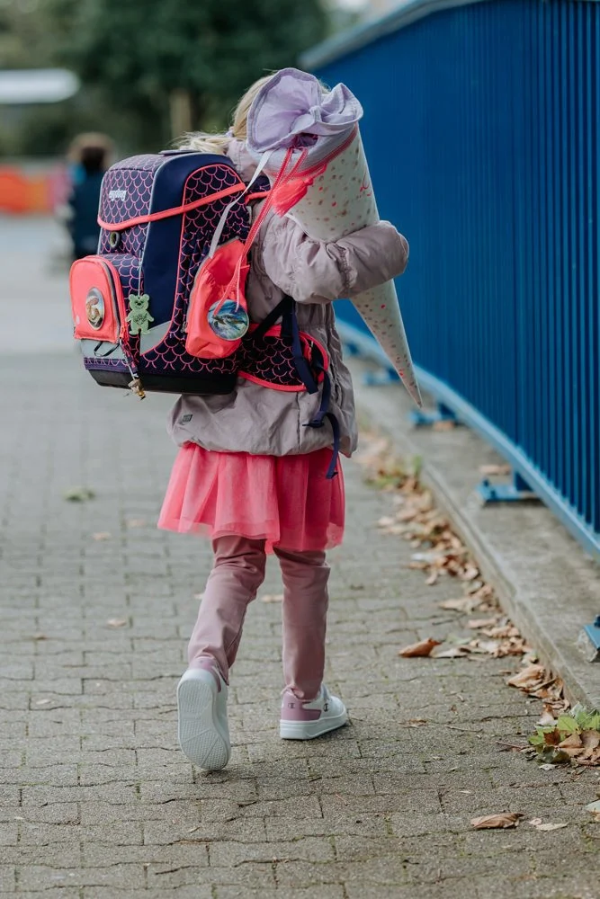 Ein Kind trägt einen Schulranzen und eine Schultüte, während es zur Schule geht.