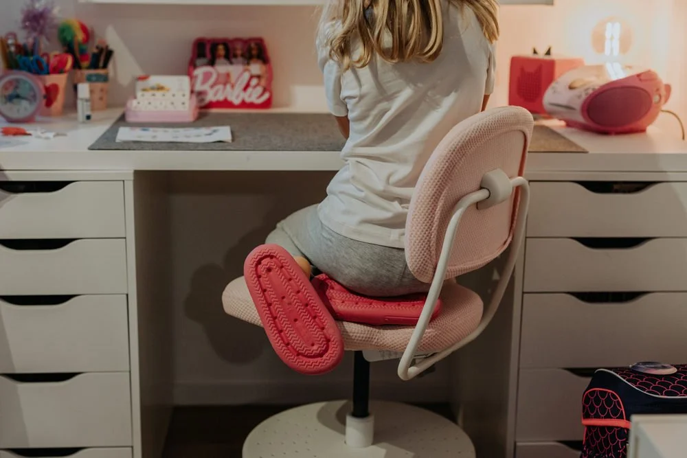 Ein Mädchen sitzt an ihrem Schreibtisch und hat pinke Hausschuhe an.