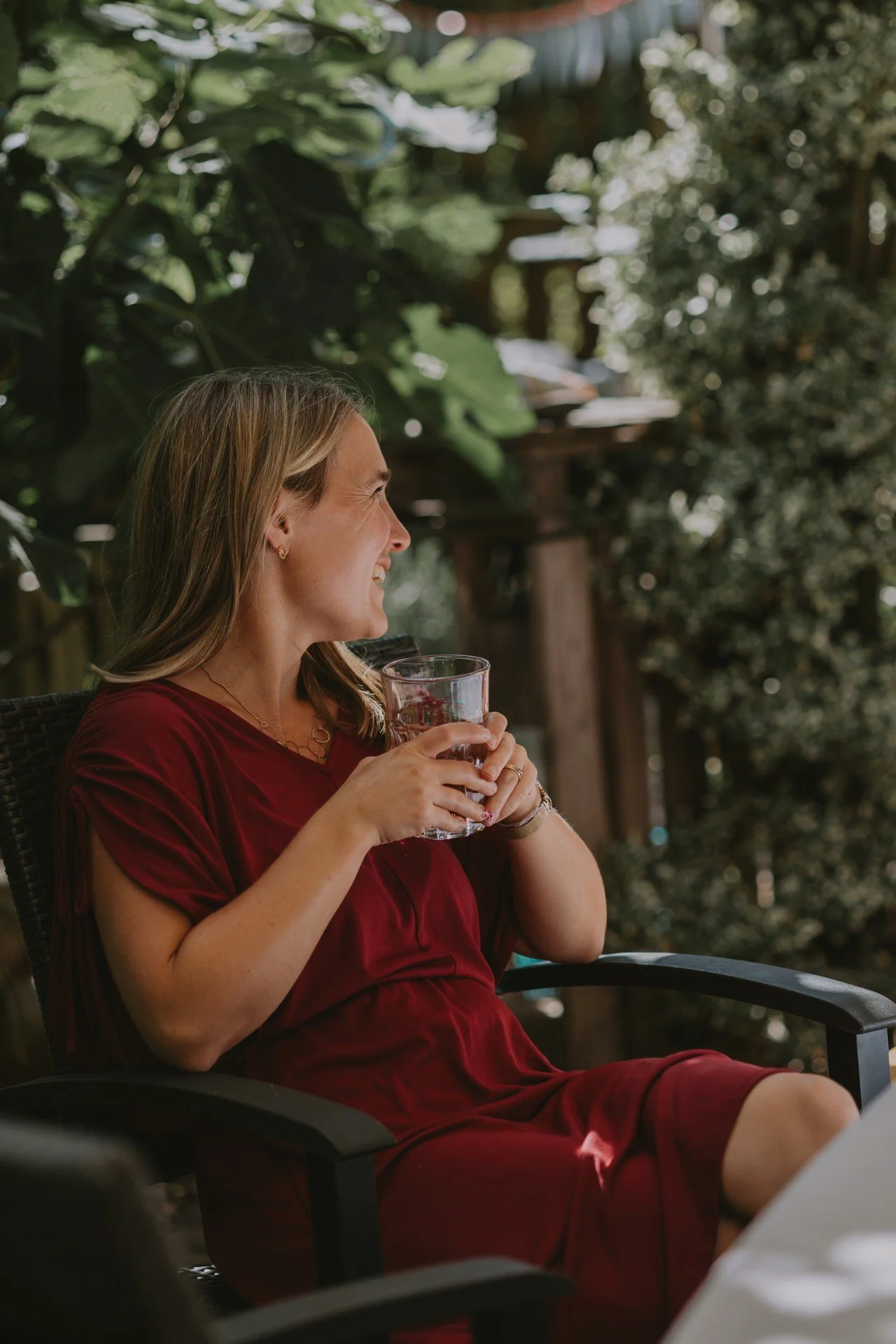 Lachende Frau genießt den Moment am Tisch im Grünen, hält ein Glas beim fröhlichen Einschulung feiern in der Pfalz.