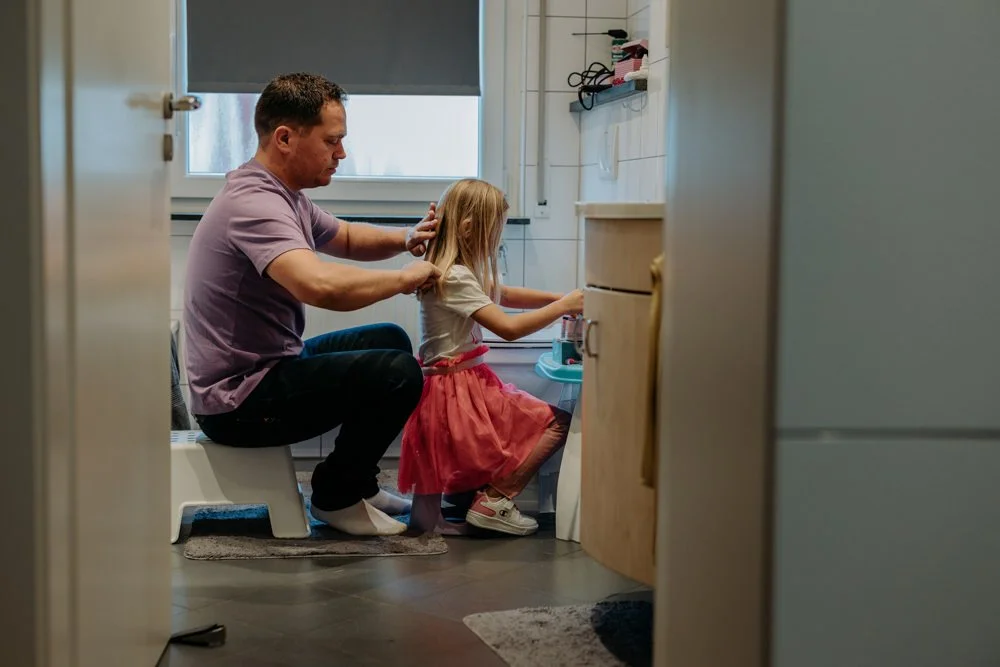 Ein Papa, der seiner Tochter die Haare bürstet, während sie im Badezimmer sitzen.