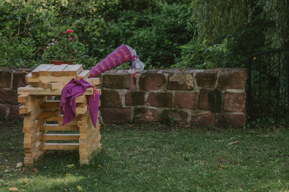 Eine selbst genähte Schultüte steckt in einem von Kindern gebauten Werk aus Holz im Garten, von einer Fotografin aus Mannheim fotografiert.