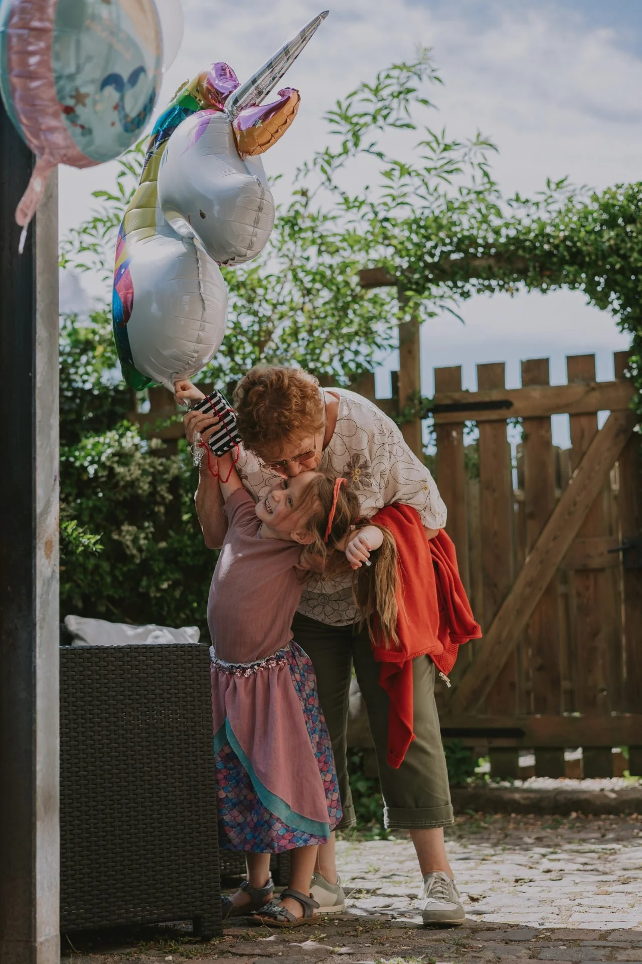 Beim Einschulung feiern in der Pfalz gibt die Ur-Oma dem Schulkind einen Kuss und schenkt einen Ballon.