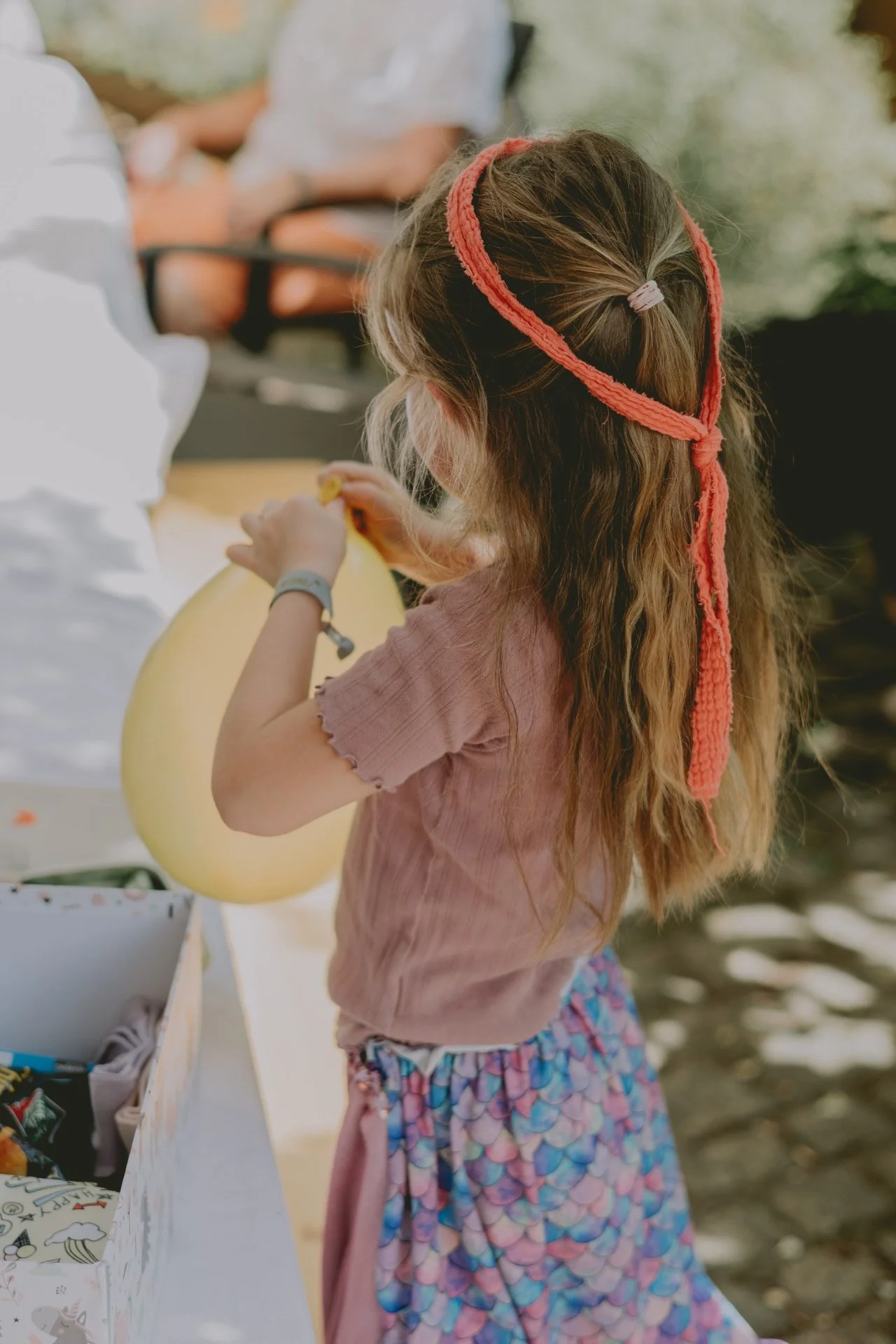 Mädchen pustet Luftballon auf für ihre Einschulungsfeier in der Pfalz, trägt selbst genähten Rock und Haarband.