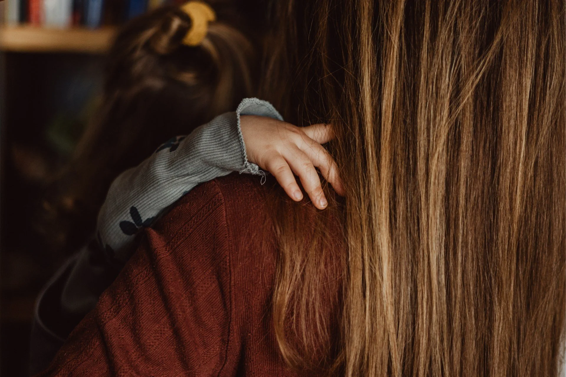 Nahaufnahme eines Kindes, das einen Arm um die Schulter ihrer Mutter legt, mit langen, dunkelblonden Haaren.