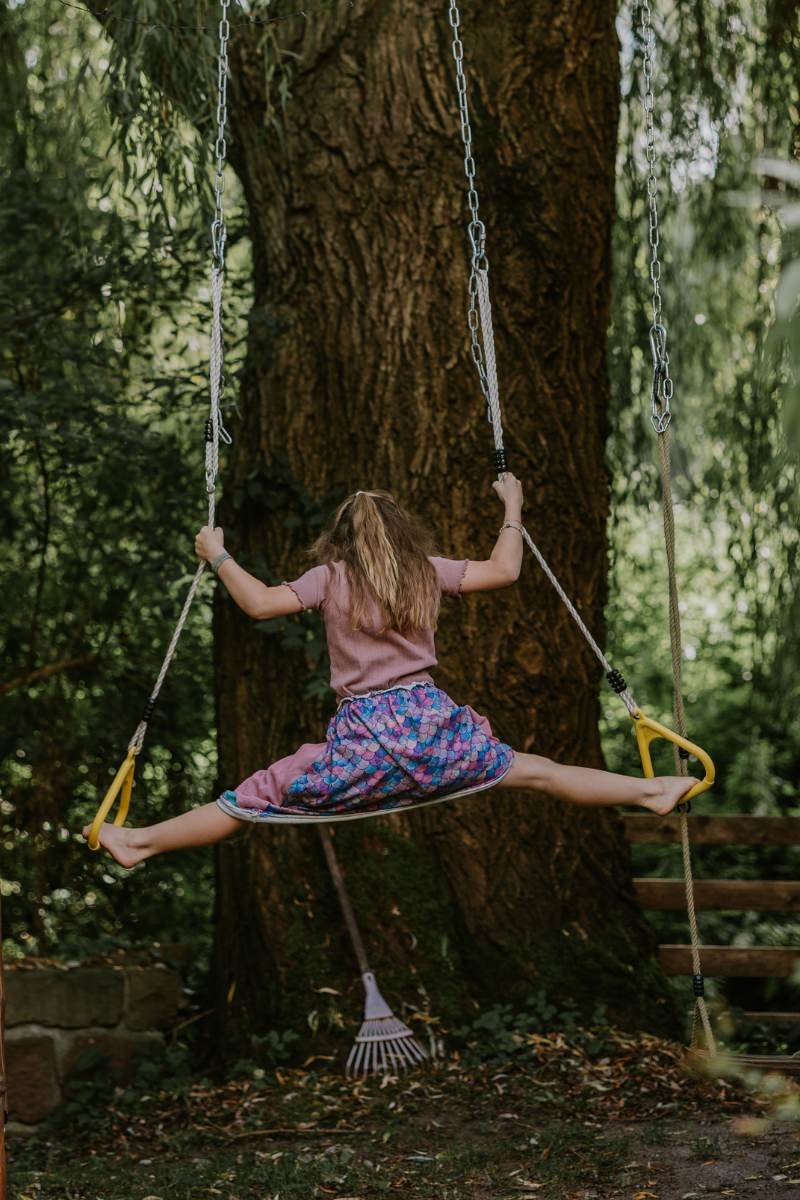 Schulkind macht Spagat an Turnringen im Garten-Klettergerüst beim Einschulung feiern in der Pfalz.