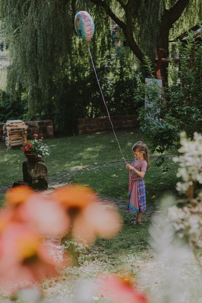 Schulkind im Garten spielt mit Ballon, umgeben von Blumen, beim Einschulung feiern in der Pfalz.
