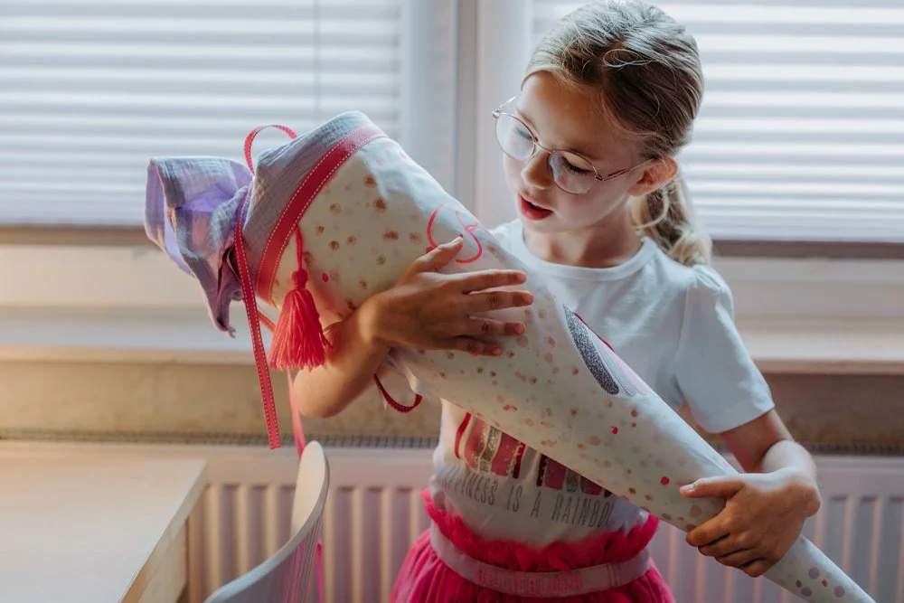 Ein Mädchen mit Brille betrachtet ihre Schultüte aus Stoff.