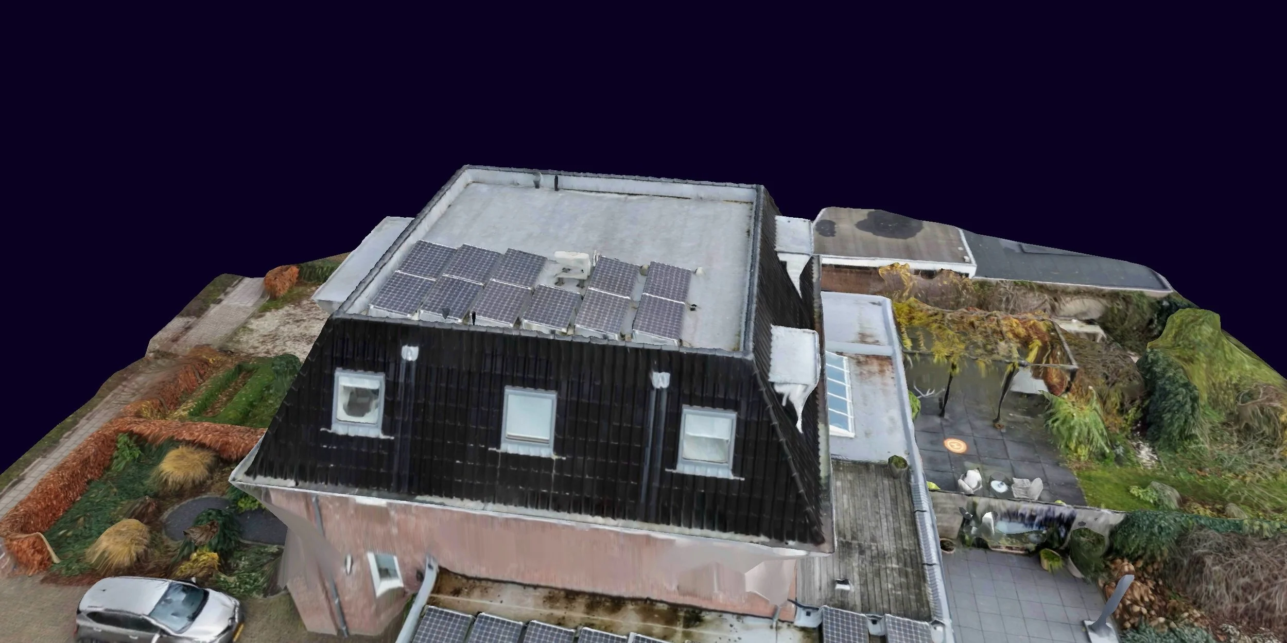 Luchtfoto van een modern gebouw met zonnepanelen op het dak, omgeven door een tuin met bomen, struiken en een terras met tuinmeubilair.