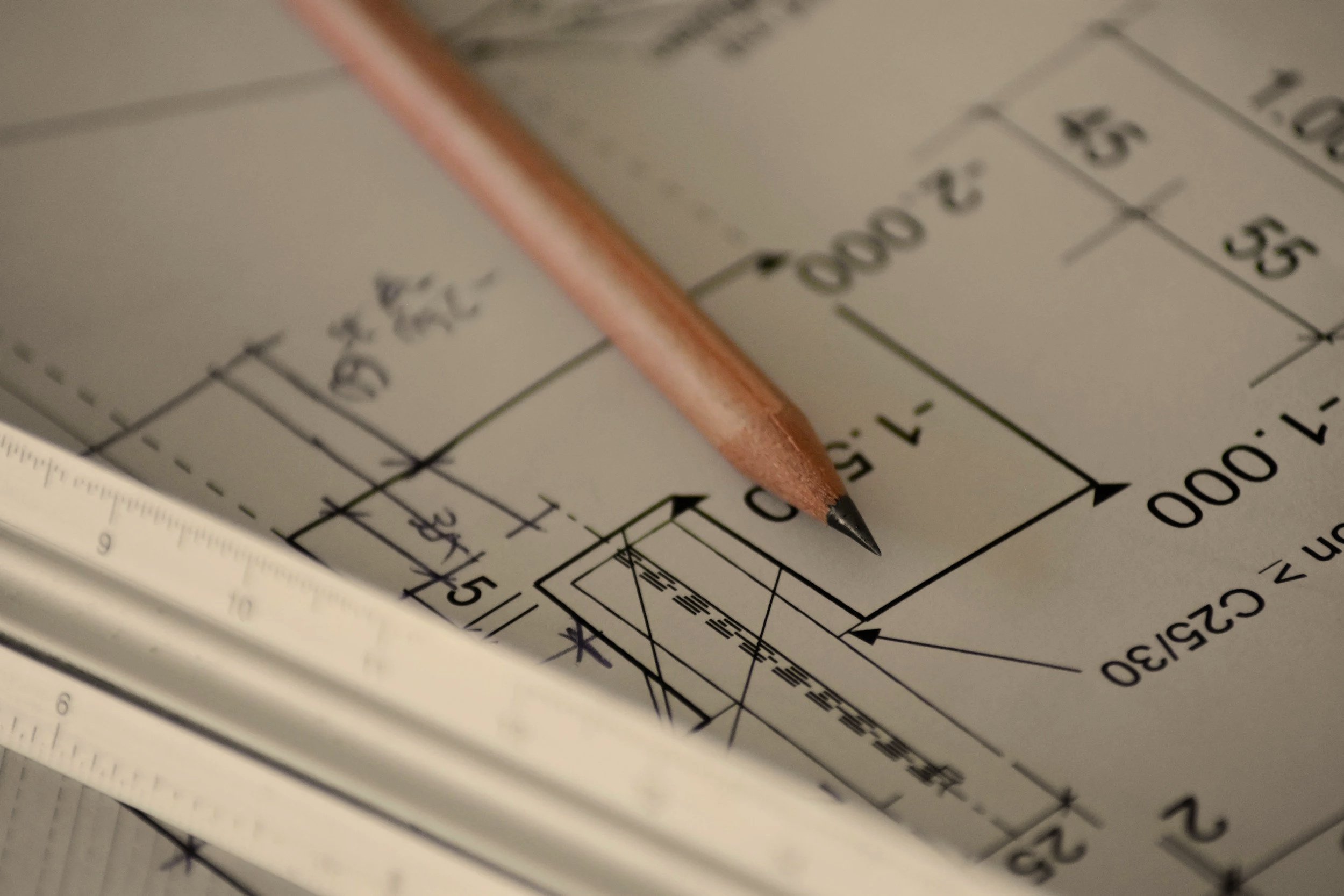 Close-up of architectural blueprints with a wooden pencil pointing to measurements and design details.