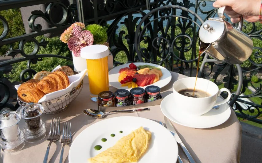 Breakfast table with croissants, omelet, fruit platter, coffee, juice, and condiments on an outdoor balcony.