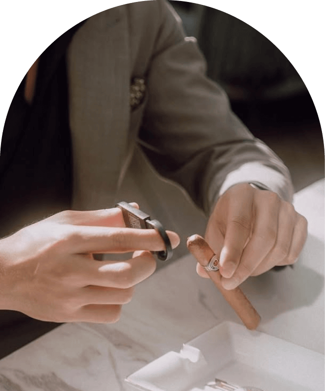 Person holding a cigar with one hand and a cigar cutter with the other on a marble surface.