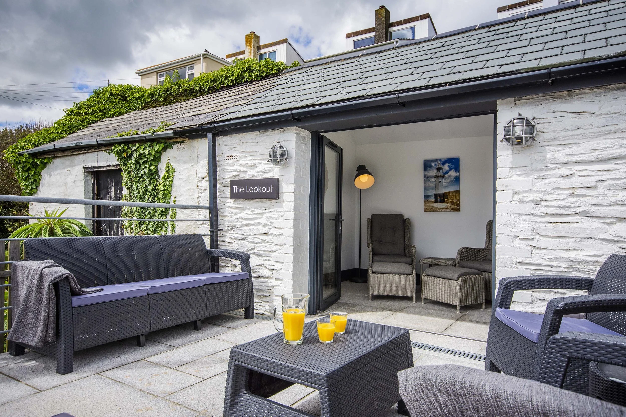 Terrace and patio of Seafarers cottage with garden room at the back with interior seating. There are garden chairs and sofas outside on the patio. 