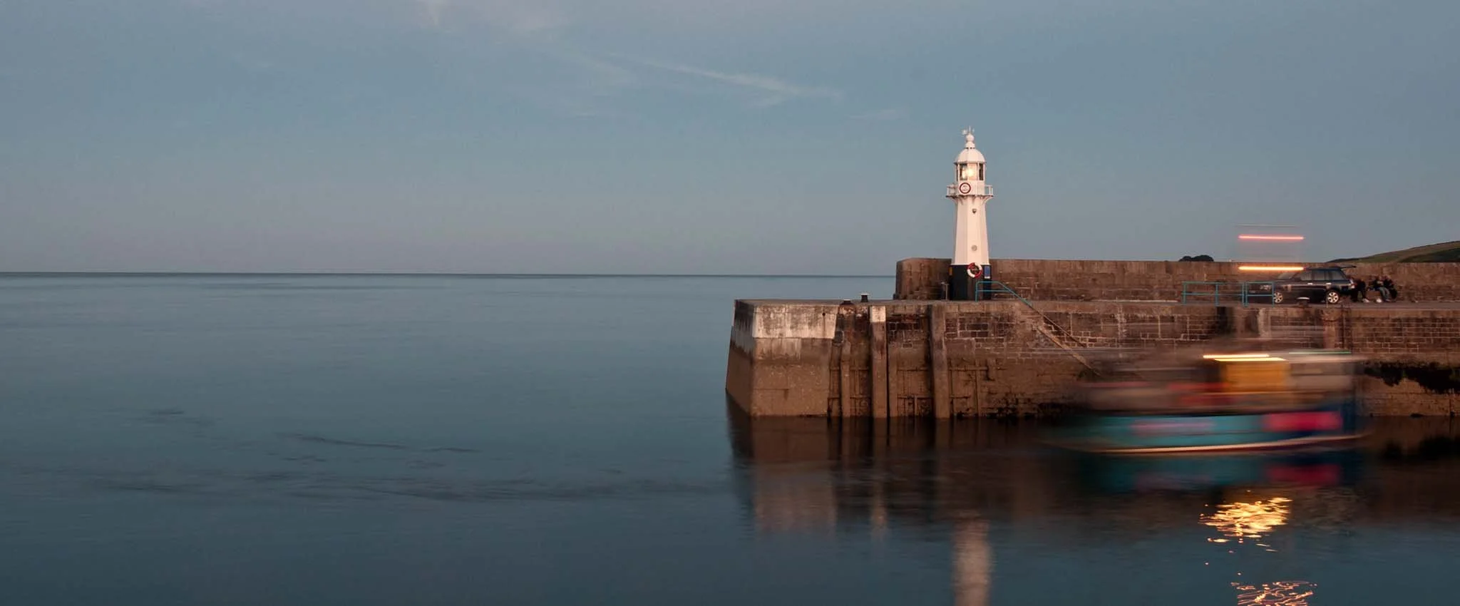 Evening view of Mevagissey Harbour with the lighthouse and fishing boat coming home. 
