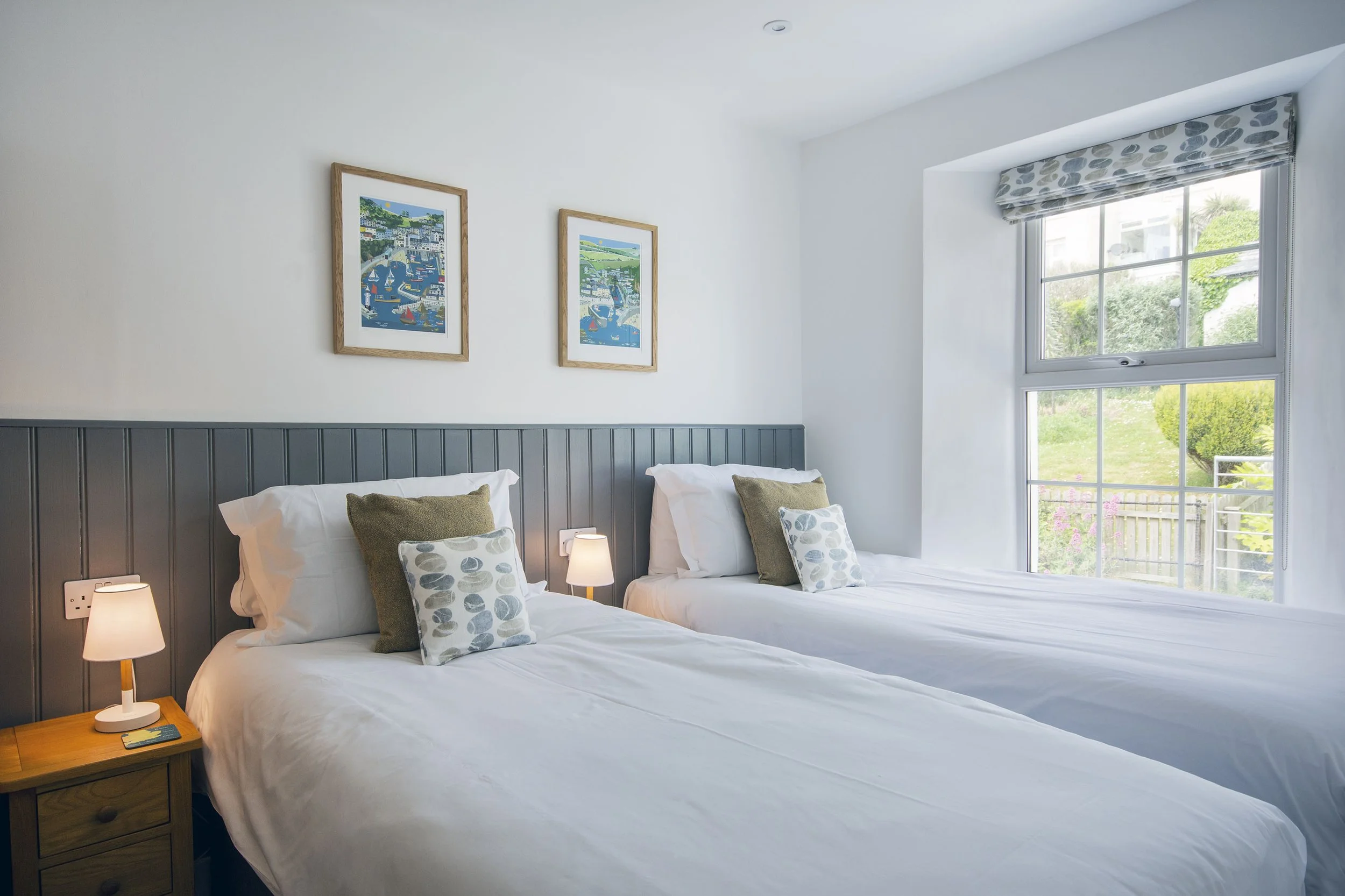 View of the twin bedroom, crisp white linens, art prints on the walls and view of the garden outside the window
