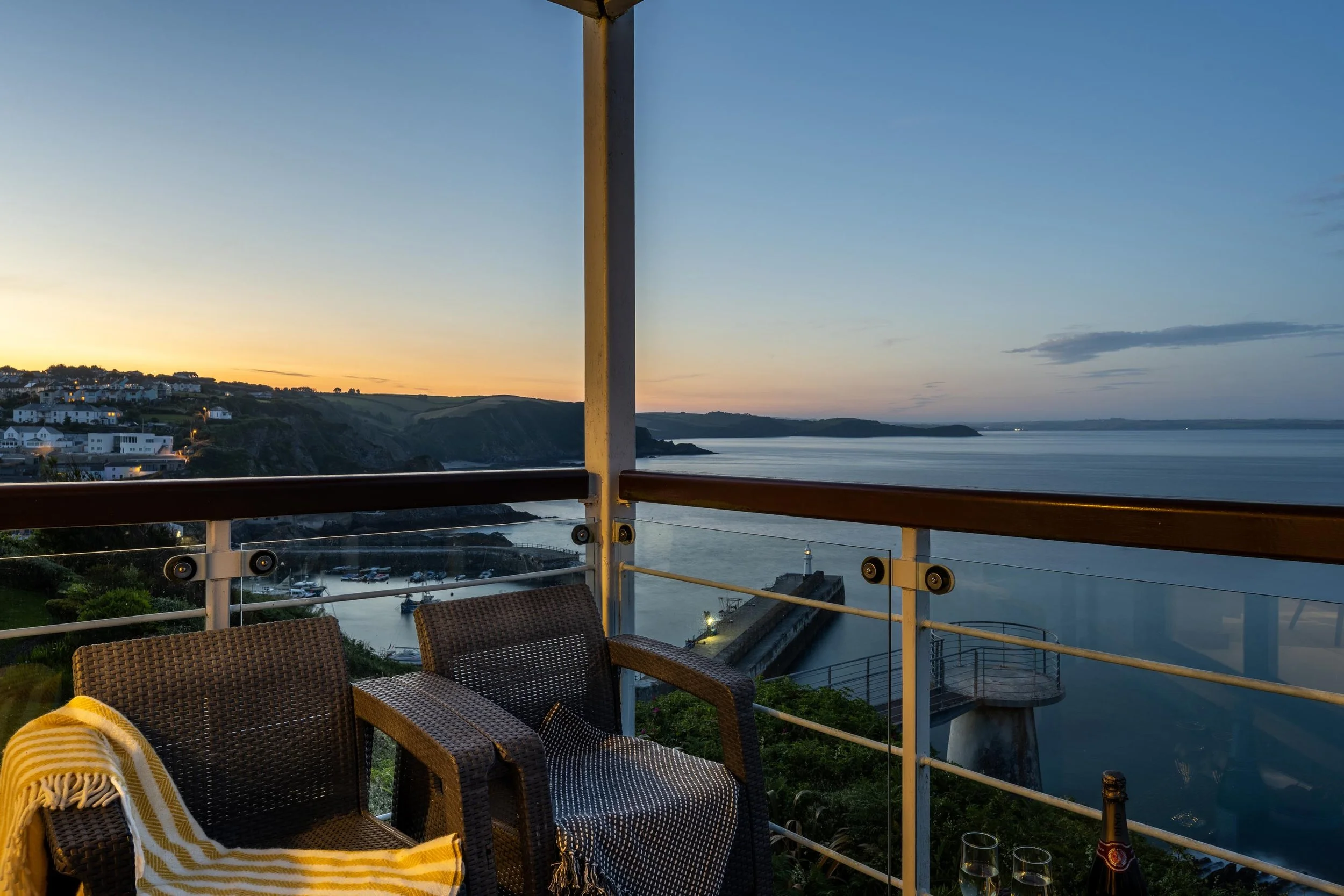 Dusk view over Mevagissey from the balcony of Marine Point. Beautiful clear sky and calm sea below. Chairs and table in the foreground with drinks. 