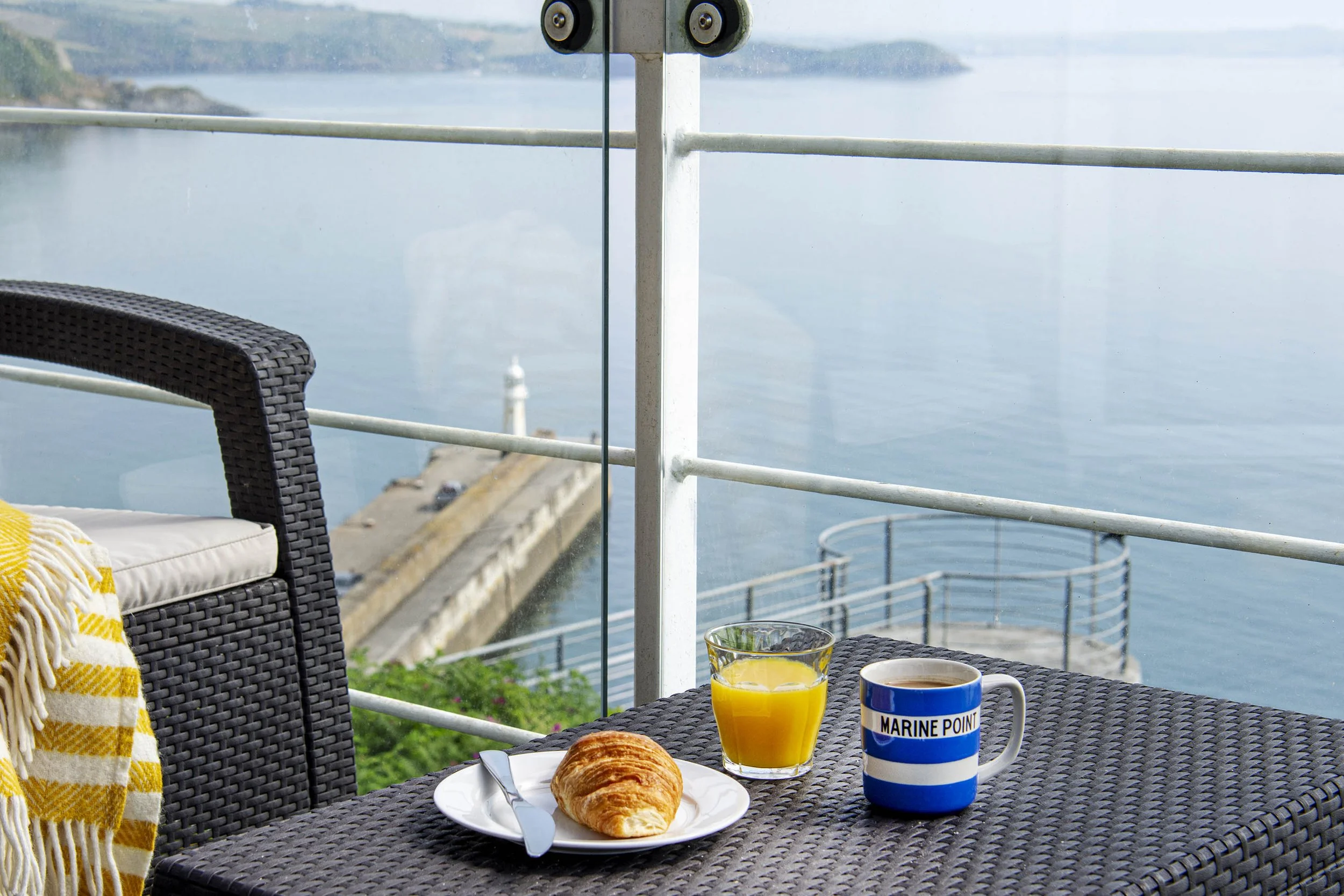 Close up view of morning coffee on the balcony of Marine Point, Mevagissey harbour in the background with coastal landscape in the distance.
