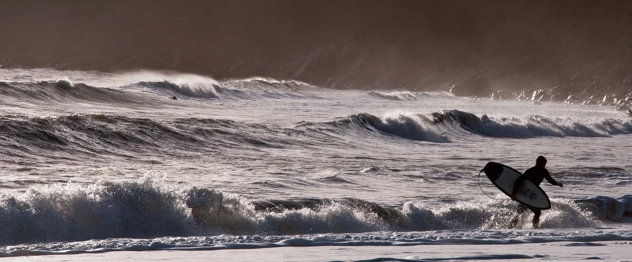 View of a surfer coming out of the sea at Vault Beach with waves in the background. 