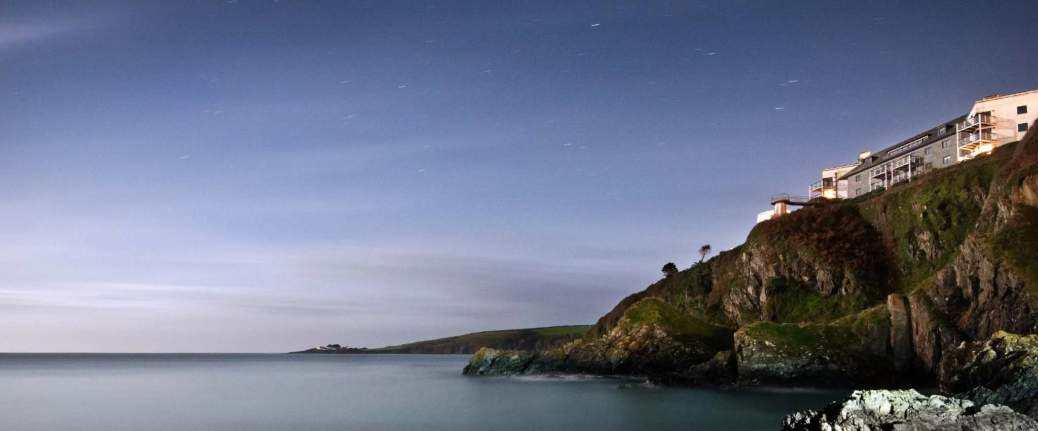 Evening view of the coastline from Mevagissey harbour with Chapel Point in the background. Up on the cliff top is Nare Court where our Marine Point apartment is located.