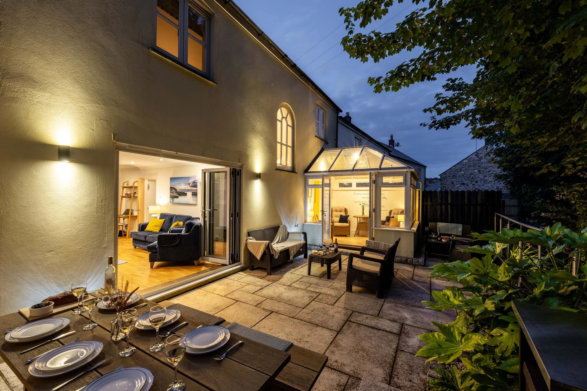 Evening view of the outdoor area of Tall Ships, with subtle lighting, table set for dinner and patio furniture with cushions.