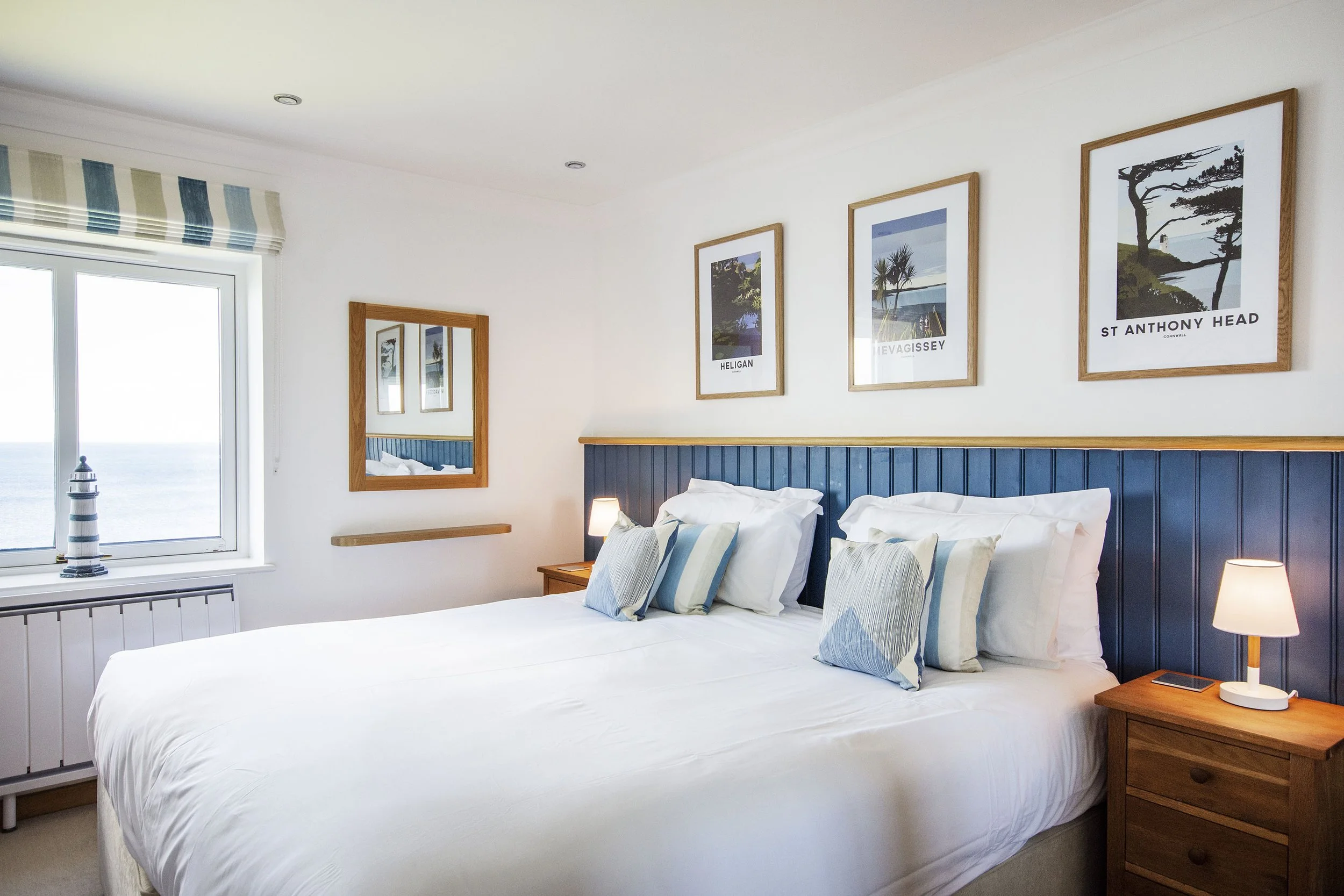 Interior view of the second bedroom with art prints on the wall behind two single beds that have been pushed together to make a double. View out the window of the sea. 