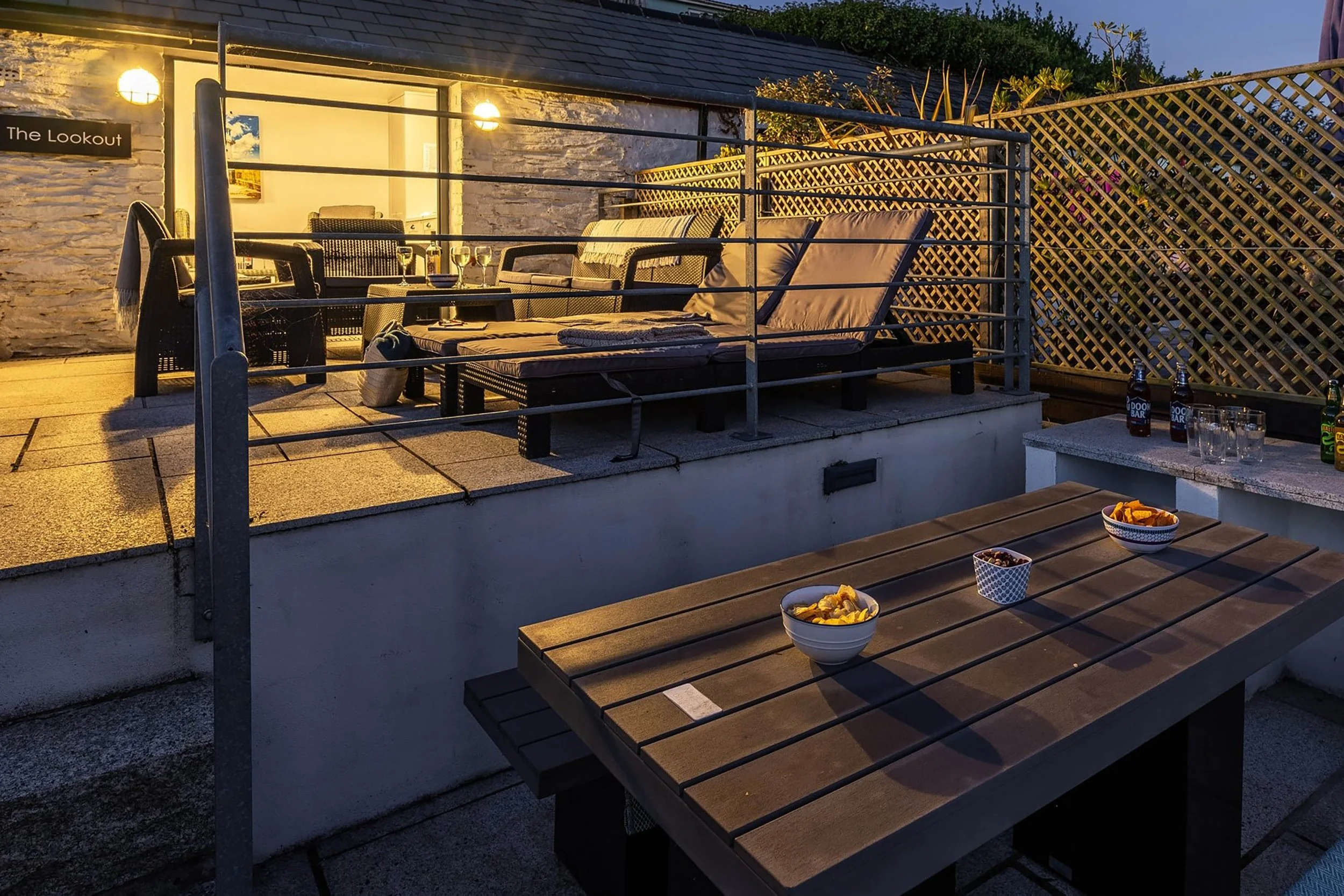 Image shows the terrace at Seafarers cottage at night time with steps, hand rails and patio with outdoor seating and garden room at the top. It is lit with subtle outdoor lighting.