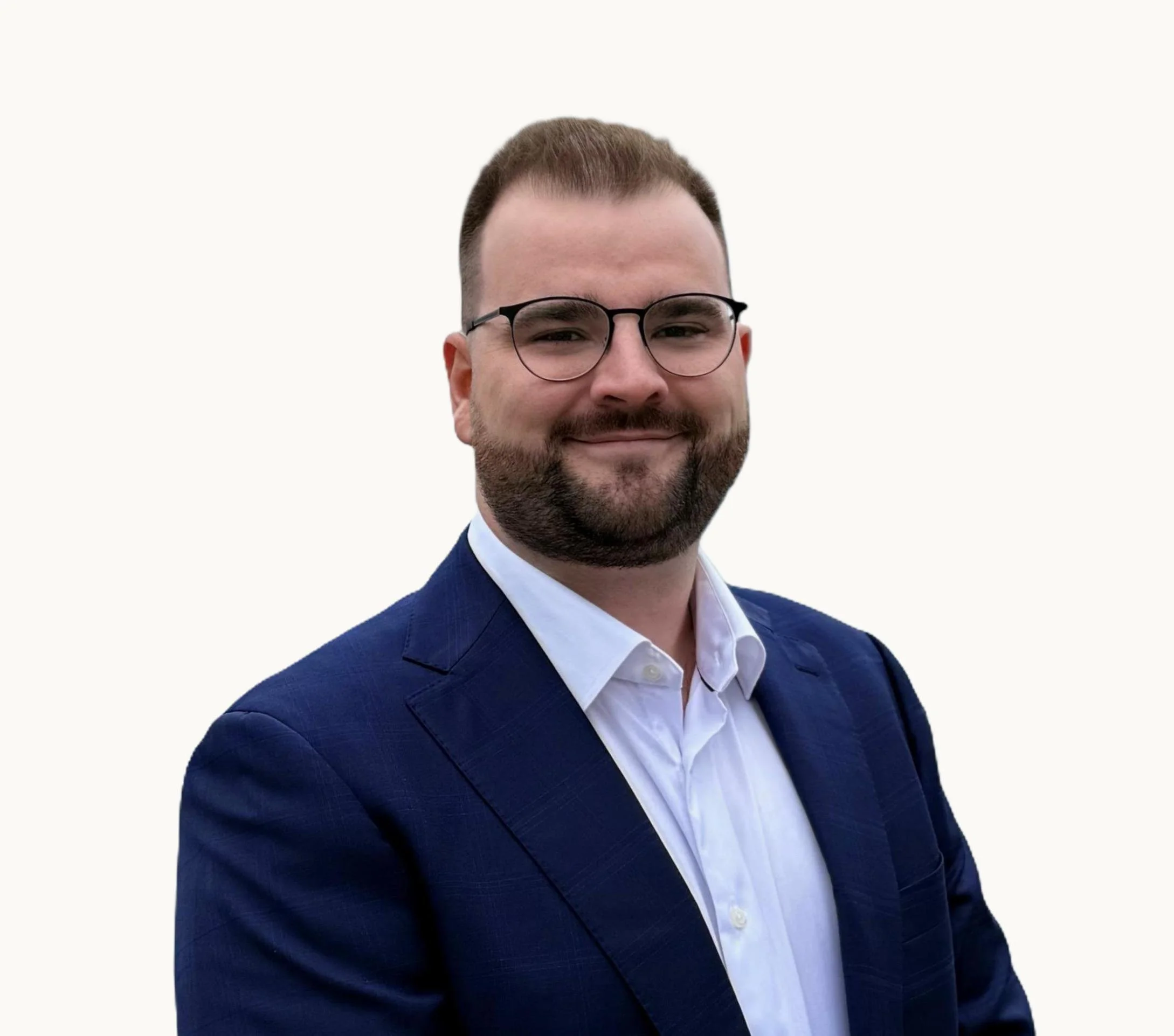 Professional man with glasses, a beard, in a suit and white shirt, smiling against a plain, light-colored background.