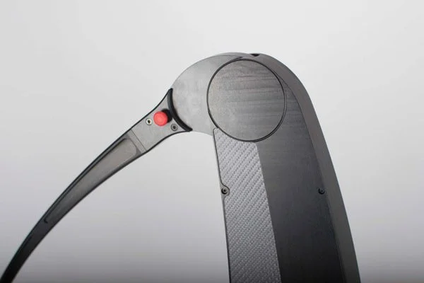 Close-up of a black electric skateboard with a round wheel and a red power button.