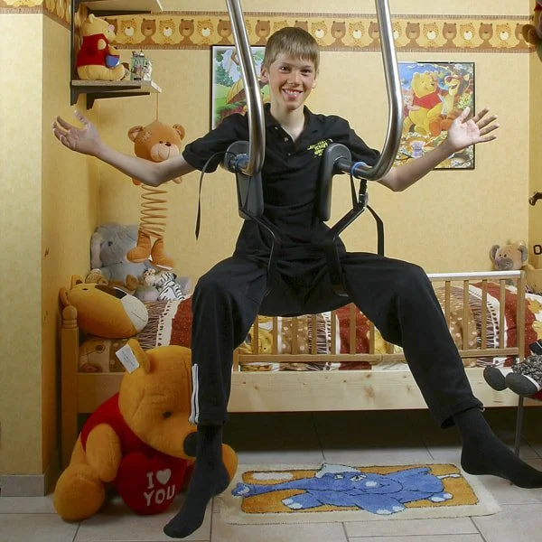 A young person sitting on gym equipment in a teddy bear-themed room, surrounded by stuffed animals and Winnie the Pooh artwork.