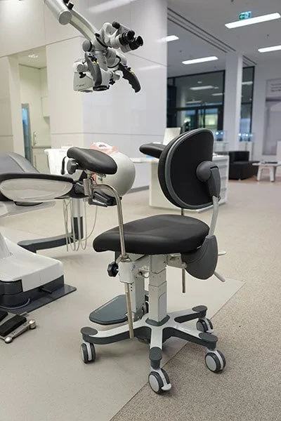 Medical chair with adjustable headrest and armrest, in a hospital or clinic setting, with a microscope overhead.