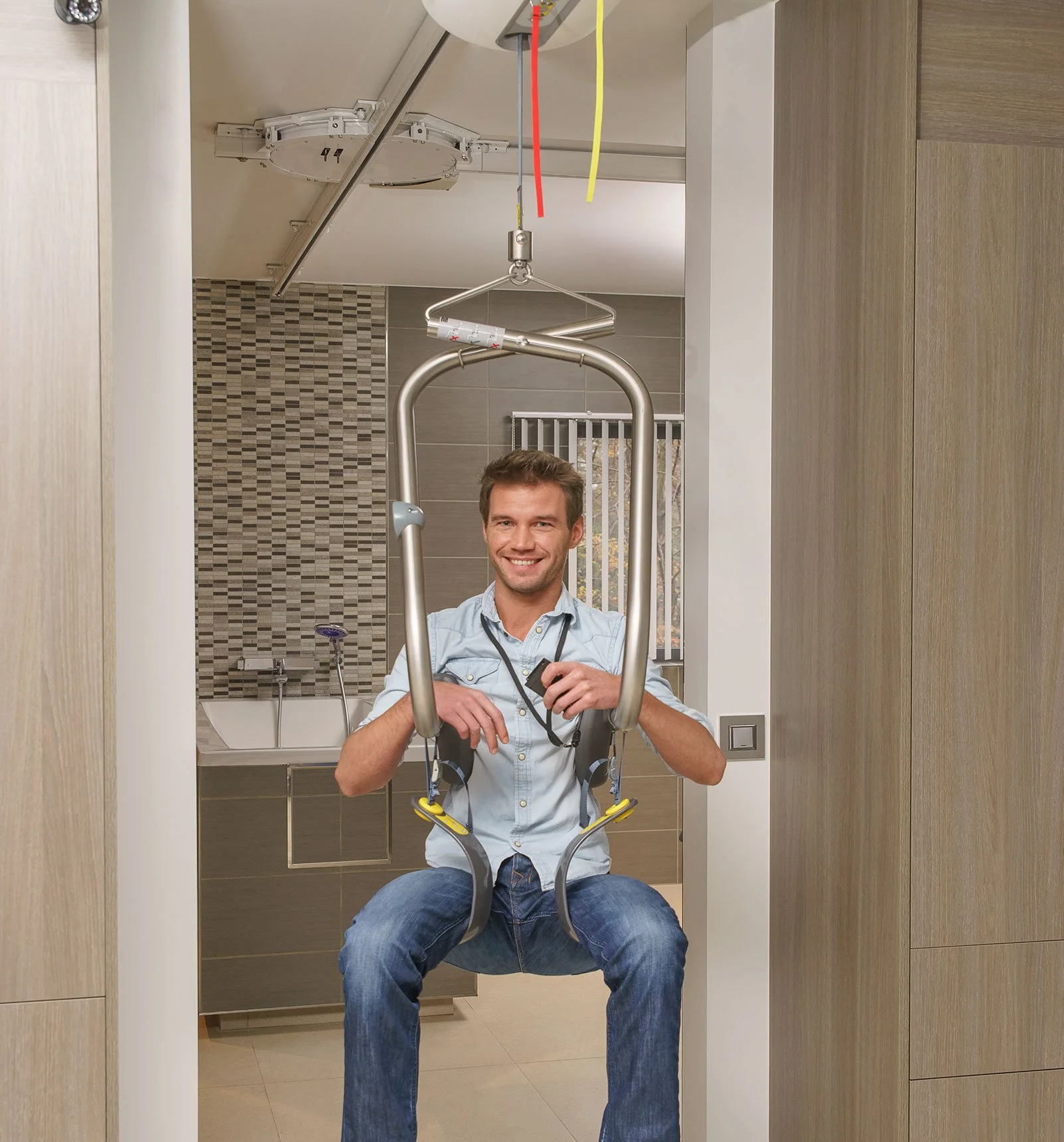 A smiling man sitting on a lift chair in a room with wooden cabinets and beige tiles, ready for a medical or dental examination.