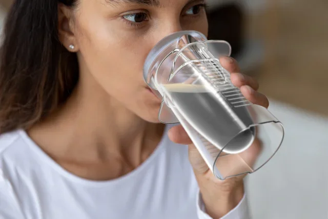 A young woman with brown hair and earrings drinking water from a clear plastic cup.