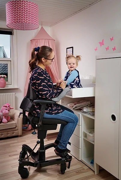 A woman sitting on an office chair, holding a young girl who is smiling, in a nursery room decorated with pink butterfly wall decals and pink ceiling lamps.