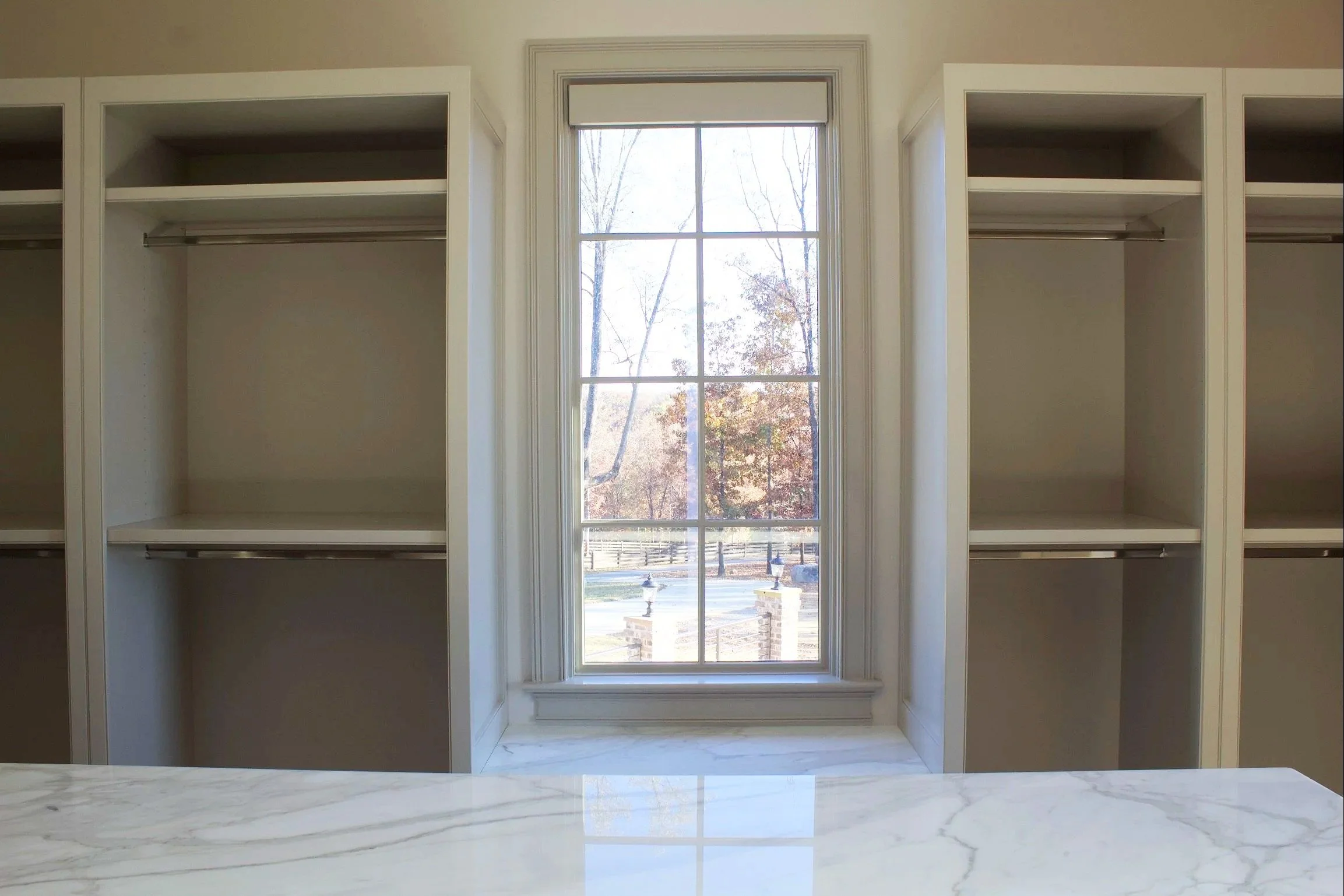 Custom closet cabinets painted Sherwin Williams Anew Gray, featuring stacked drawer island, window seats, hidden closet behind mirror, and natural stone counter tops by Crawford Cabinets