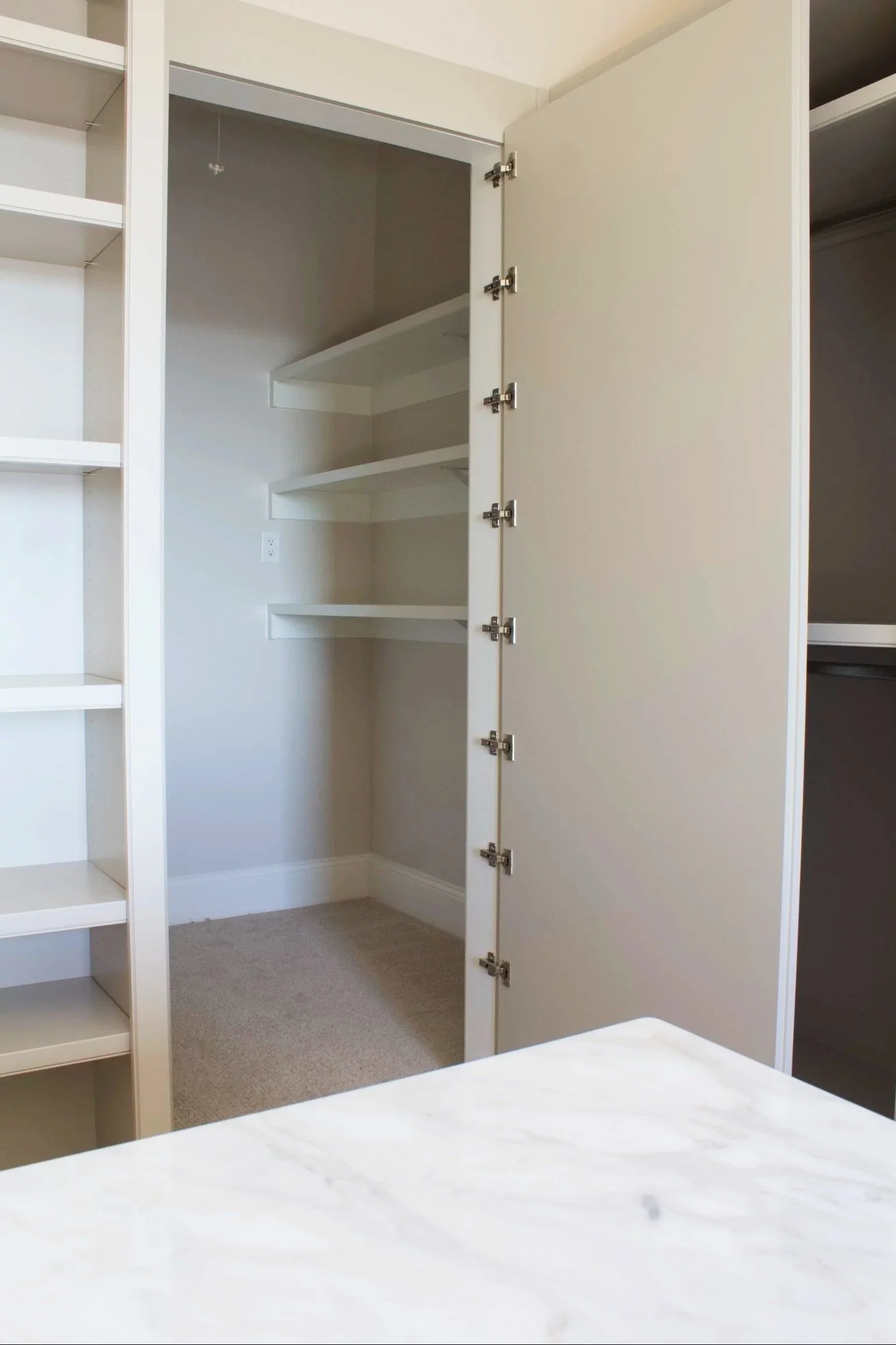 Custom closet cabinets painted Sherwin Williams Anew Gray, featuring stacked drawer island, window seats, hidden closet behind mirror, and natural stone counter tops by Crawford Cabinets