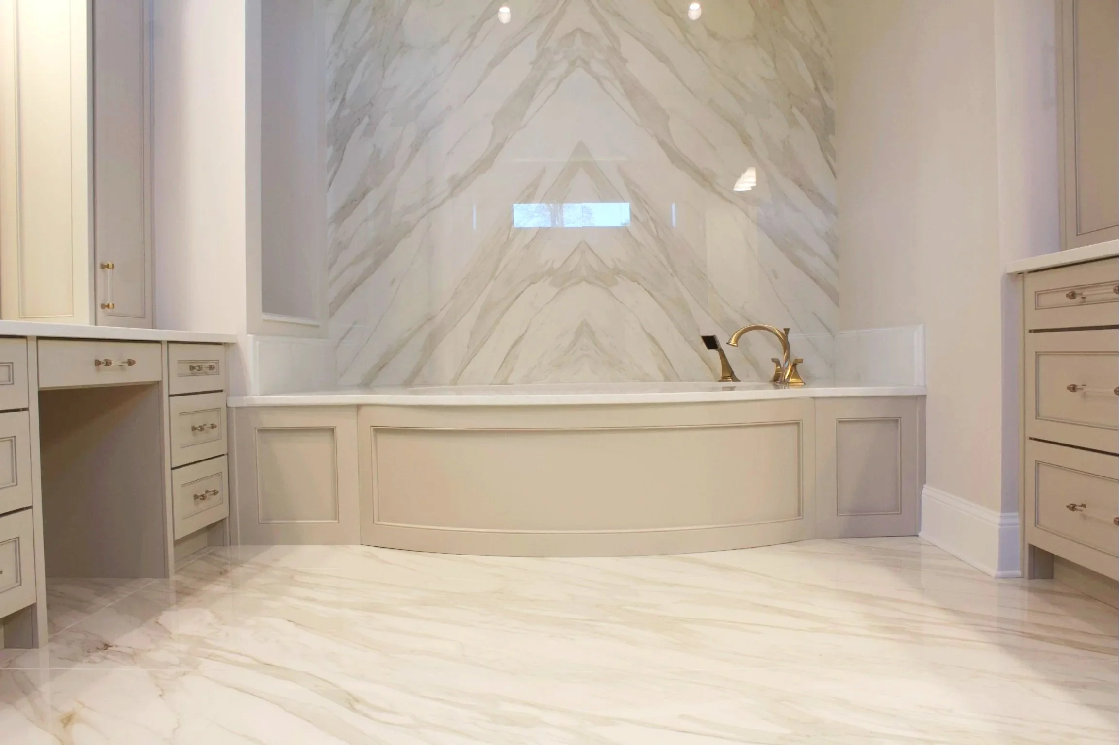 Custom curved tub front painted Sherwin Williams Anew Gray, featuring natural stone countertops by Crawford Cabinets