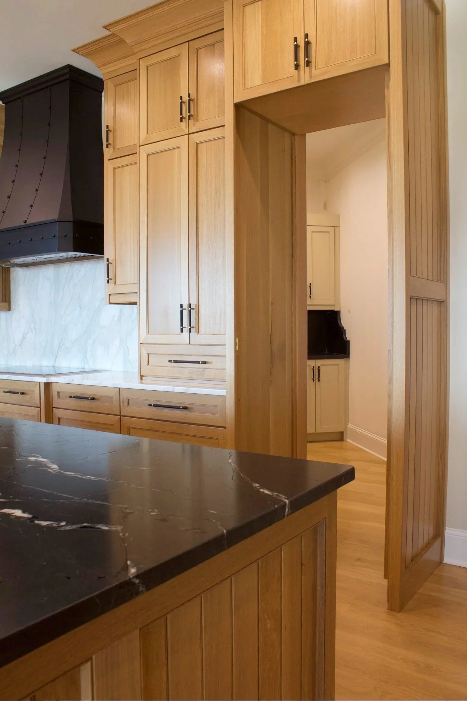 Custom hidden pantry cabinets painted Sherwin Williams Accessible Beige, featuring open shelves and natural stone counter tops by Crawford Cabinets
