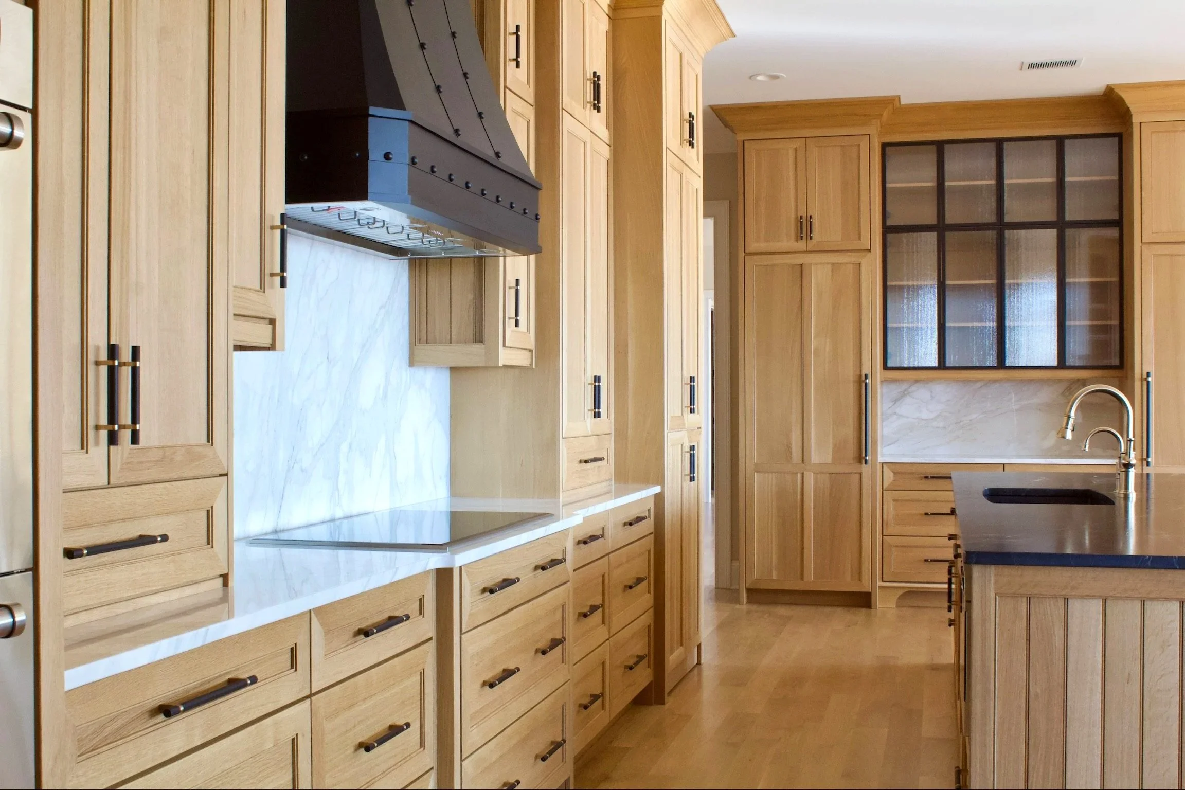 Custom White oak kitchen with modified end panels, reeded glass doors, hidden pantry, natural stone countertops, and natural finish by Crawford Cabinets