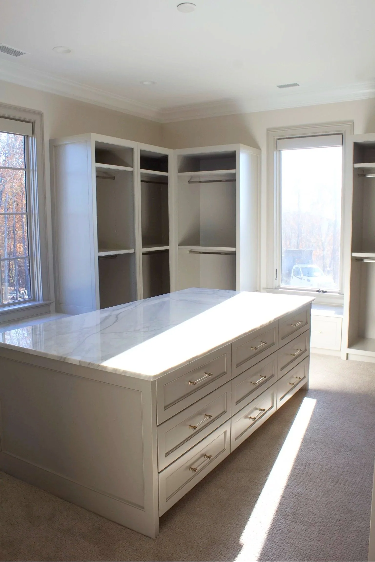 Custom closet cabinets painted Sherwin Williams Anew Gray, featuring stacked drawer island, window seats, and natural stone counter tops by Crawford Cabinets