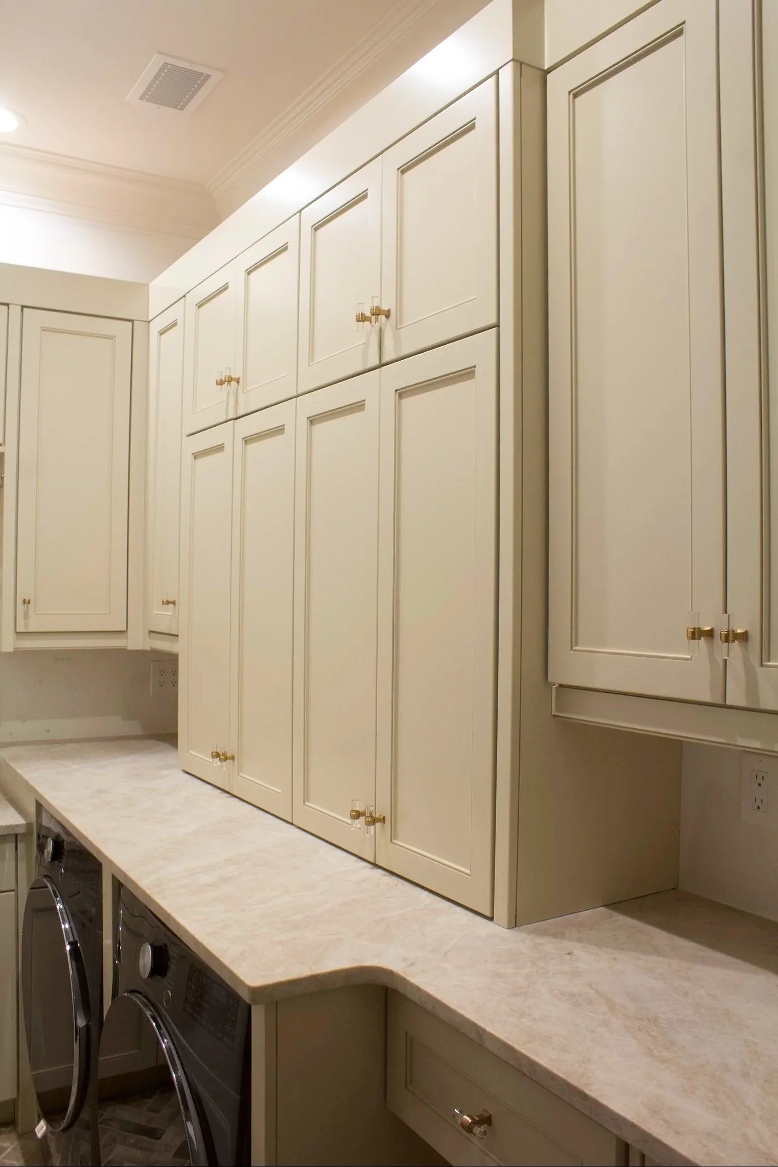 Custom Laundry room cabinets painted Sherwin Williams Accessible Beige with under counter washer and dryer, sink, closet rod and natural stone counter tops by Crawford Cabinets